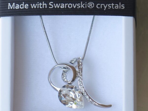 Ogrlica od Swarovski elemenata s kristalom prozirno-bjelkastih nijansi i iskričavog sjaja. Ima oblik suze, a obavijen je vijugom srebrne boje